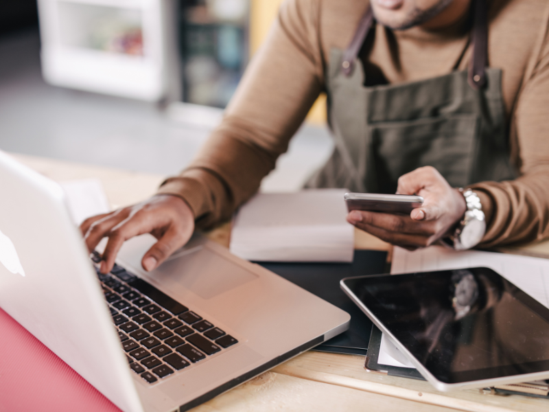 Business owner managing payroll and finances on a laptop and smartphone, emphasizing the importance of efficient payroll solutions for small businesses.