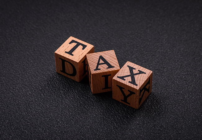Is Workers Comp Taxable_ - PEOPayGo Wooden letter blocks arranged to spell 'TAX DAY' on a dark textured surface, conveying tax season.