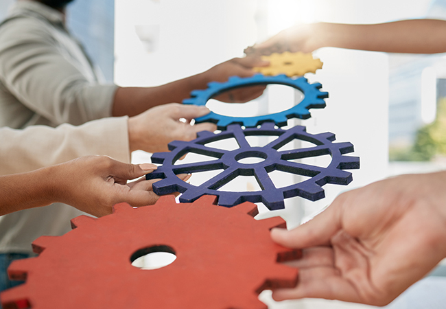 Servicios PEO para Pequeñas Empresas Beneficios Costos Mejores Proveedores - PEOPayGo Multiple hands fitting together to connect colorful interlocking gears, symbolizing teamwork and collaboration.