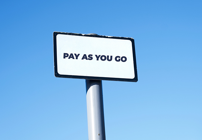 Pay As You Go Workers Comp How It Works - PEOPayGo - PEOPayGo Road sign reading 'PAY AS YOU GO' mounted on a pole against a bright blue sky.