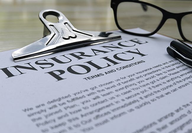 What Is Indemnity Insurance_ When Do You Need It_ - PEOPayGo - PEOPayGo Close-up of an insurance policy document titled 'INSURANCE POLICY' with a clipboard, glasses, and a pen nearby.