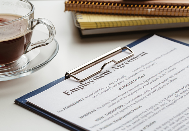 What Is a Registered Employment Agreement_ - PEOPayGo - PEOPayGo Employment agreement on a clipboard with a cup of coffee and notebooks on a desk.