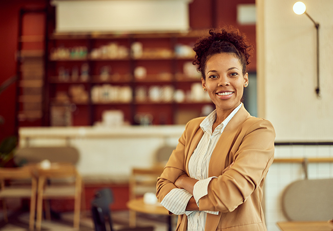 Workers Comp for Sole Proprietors Do You Need It_ - PEOPayGo - PEOPayGo Smiling businesswoman with arms crossed in a cafe or restaurant setting.